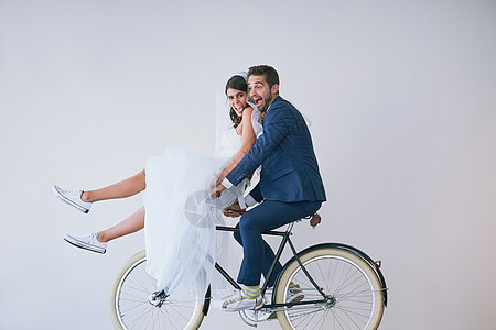 与我同在的情侣一起享受人生 一对新婚年轻夫妇在灰色背景下骑着自行车工作室肖像片图片