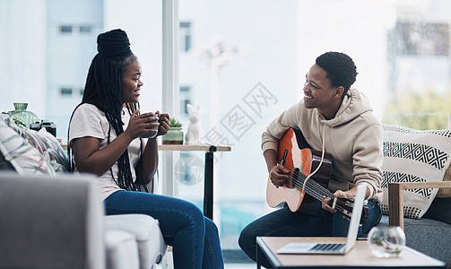 一个年轻男人弹吉他 而妻子在家喝咖啡时 却在玩这把吉他图片