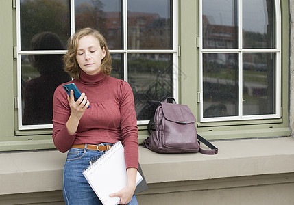 焦虑的女学生在等待某人和阅读智能手机信息时等待着图片