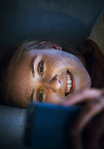 女人 晚上在家里或家里的客厅里打电话或躺在沙发上玩在线约会应用程序 社交媒体或互联网电子竞技游戏 在移动技术社交网络新闻上微笑 图片