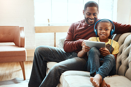 一起嗨表情包平板电脑 沙发和父亲与他的儿子在社交媒体上观看有趣的漫画或表情包视频 快乐 微笑和非洲男人与他的男孩一起在移动设备上播放电影 同背景