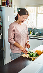 现在开始吃健康的食物 一位年轻女子在家里厨房切蔬菜 (笑声)图片