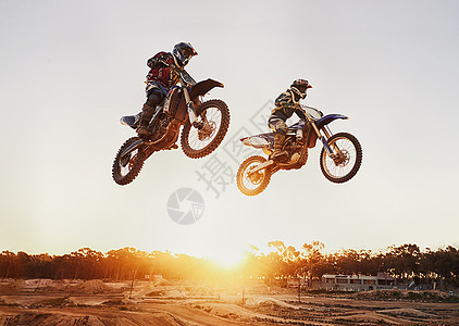 在日落时跳跃 在比赛中 有两个骑摩托的车手在半空图片