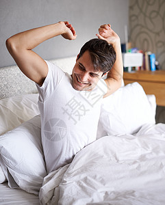 伸展着那些困睡的肌肉 一个年轻男人醒来时在床上躺着图片