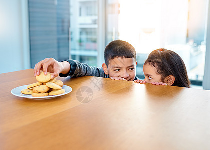 看看我得到了什么让我们享受 两个淘气的小孩在厨房桌子上偷饼干 在家里吃饼干图片