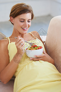 一个放松的孕妇坐在沙发上 享受健康沙拉 然后坐到沙发上图片