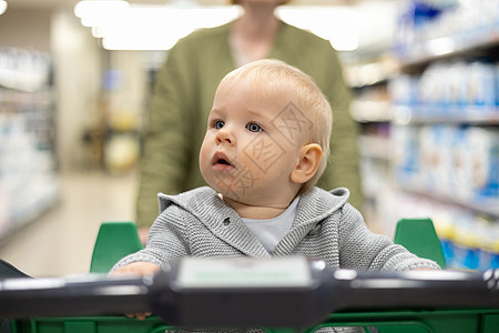 母亲在超市杂货店的百货街道上与婴儿男孩一起推着购物车 用孩子来买东西的概念产品妈妈市场购物店铺走道服务顾客大车婴儿车图片
