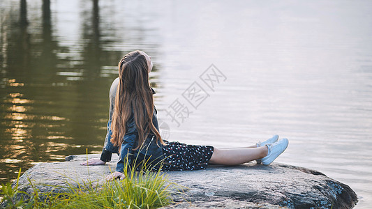 一个女孩坐在湖边的岩石上假期女士远足幸福公园阳光黑发晴天冒险天空图片