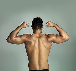 他是一个钢铁人 一个运动的年轻运动员用灰色背景 伸展肌肉的回视镜头图片