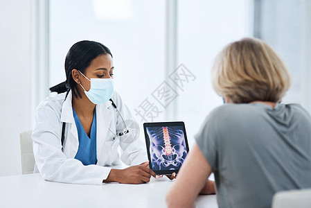 从诊断到预后的一流患者护理 一位年轻医生在与一位年长女性会诊时使用数字平板电脑图片