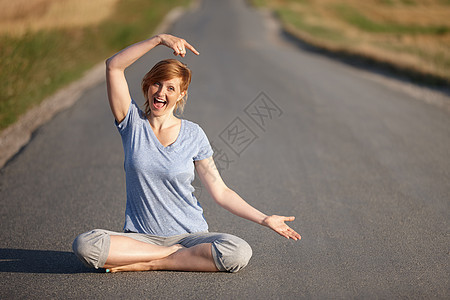 她找到了通向整体福祉的道路 在乡村道路上坐在莲花姿势上看着兴奋的一位女性的肖像 (笑声)图片