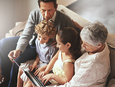 技术将年轻人和老年人聚集在一起 一对老年夫妇和他们的孙子们坐在一起使用笔记本电脑图片