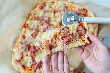 多汁可口的披萨片 配火腿 洋葱和奶酪 在背景上的披萨刀 在家做披萨 女孩手里拿着一块披萨图片