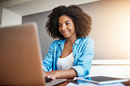非洲女人我在家工作时总是很开心 在家里用笔记本电脑工作着一个有吸引力的年轻女人背景