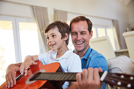 和爸爸一起弹奏曲子 一位父亲和他年幼的儿子一起坐在家里的客厅里弹吉他图片