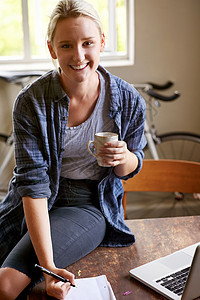一位年轻女士坐在桌子上喝咖啡时 在一张纸条上写下一些东西的笔记本图片