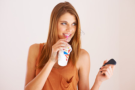 喝酒和发短信 一个年轻女人拿着手机喝苏打水时喝汽水图片