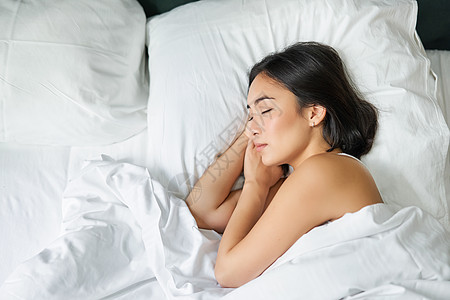 亚洲女性独自睡在白色枕头上的特大号床上的顶视图图像 小女孩闭着眼睛躺在卧室里 早晨的阳光照在房间里午睡毯子时间成人寝具女士床单就图片