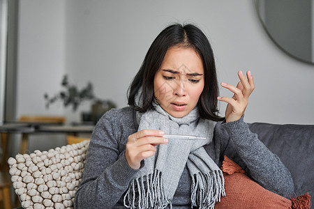 惊吓的女人看着她的温度计 感寒 发烧 坐在家中休病假等女士温度流感疾病感染沙发过敏弱点药品互联网图片