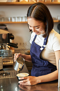 喝咖啡倒蒸牛奶的咖啡店工作人员 为拿铁艺术准备卡布奇诺Cappuccino 站在柜台后面的蓝色围裙商务拿铁职场职员命令咖啡人士学图片