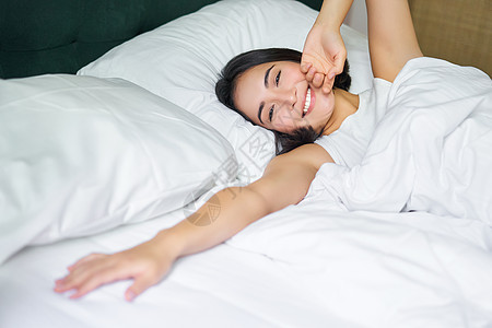 浪漫的亚洲女孩在舒适的卧室里醒来 躺在白床单床上 将手伸向空枕头毯子寝具女士小憩就寝午睡房间成人时间房子图片