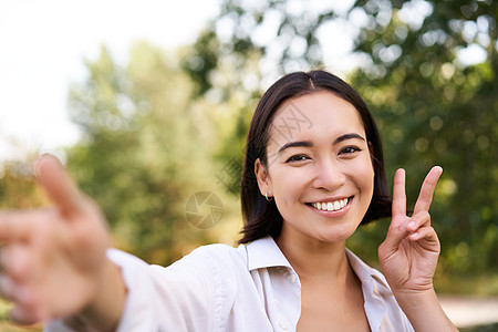 快乐的亚洲女人在公园里玩自拍 在智能手机上拍照 微笑和看着喜悦女性自由女孩黑发假期享受治疗学生福利图片