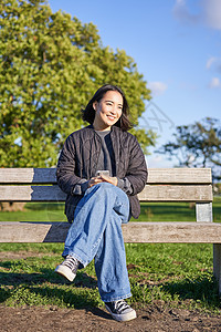 美丽的黑发女人用智能手机坐在长椅上等待某人使用移动应用程序的垂直照片图片