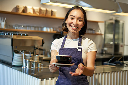 微笑的亚洲女性肖像拿着咖啡 在咖啡馆为客户准备饮料 工作和提供饮料 穿着制服围裙服务员工人命令食物商务杯子成人顾客生意员工图片