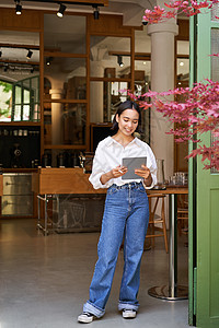 站在咖啡厅入口前的女服务员 向餐厅里带平板电脑的宾客邀请一对餐饮客人调酒师商务人士咖啡师酒吧成人商业女孩员工咖啡图片