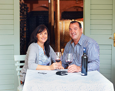 红酒酒窖没有一瓶葡萄酒 浪漫的夜晚是不完整的 一对快乐的成熟夫妇坐在酒窖的桌子旁 用红酒敬酒的肖像背景