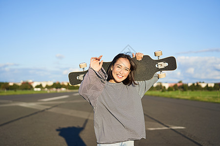 休闲和人 快乐的亚洲女人站在长板上 在乡间空荡荡的路上巡航 溜冰女孩拿着她的滑板 对着镜头微笑青少年滑冰行动潮人运动女士闲暇溜冰图片