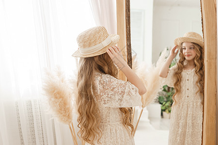 长发的美少女在镜子前戴上草帽 对金发女郎的自以为是的感觉拥抱配件衣服干草达人女士装饰稻草洞察力青少年图片