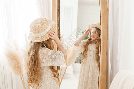 长发的美少女在镜子前戴上草帽 对金发女郎的自以为是的感觉配件裙子身体干草头发装饰风格达人青少年验收图片