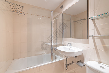 宽敞的浴室配有柔软的桃色墙 小水槽和方形镜子 旁边是白色马桶 上面是放置各种配件的玻璃架子 另一边是洁白干净的浴缸图片