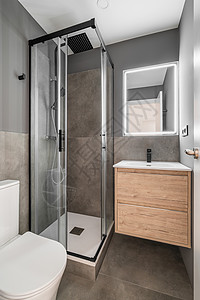 现代设计的小浴室 灯光明亮 淋浴间由符合人体工程学的玻璃制成 配有黑色水龙头 带木抽屉和白色水槽的梳妆台与整体设计相得益彰图片
