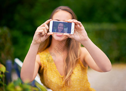 一个无忧无虑的年轻女子在公园用手机拍自拍 校对 Portnoy图片