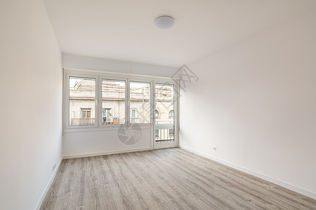 一间空旷明亮的房间 铺有灰色木地板 白色的墙壁在视觉上使房间更大 客房设有窗户和门 可通往小阳台 并享有对面房屋的景致图片