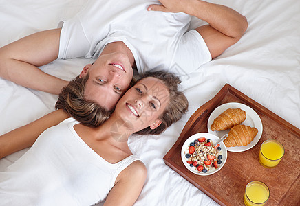 在床上享受慵懒的早餐 一对年轻夫妇躺在床上吃早餐并抬头的剪影图片