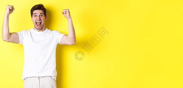 激动人心的男子获胜 举起手来庆祝 为团队赢得胜利和扎根 站在黄色背景之上的画面成就成功优胜者微笑情绪商业快乐工作室胡须潮人背景图片