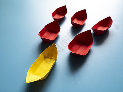 领头概念 - 黄色纸质折纸船 以蓝封面背景领导红纸船的其余部分 商业和复制空间图片