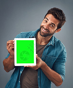 摄影棚拍到一个英俊的年轻人 在灰色背景下 展示了一张绿色的数码平板电脑 他戴着绿屏 (笑声)图片