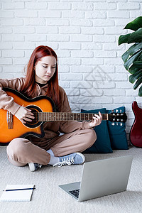 年轻女子在家弹吉他时学习在家里弹吉他歌曲砖墙快乐女性闲暇头发乐趣技术吉他手音乐家图片