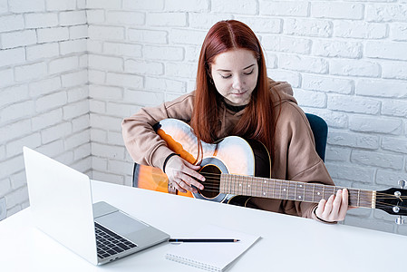 年轻女子在家弹吉他时学习在家里弹吉他音乐青少年女士电脑歌曲闲暇音乐家砖墙快乐成人图片