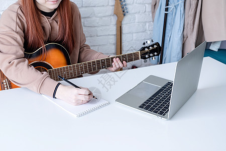 年轻女子在家弹吉他时学习在家里弹吉他砖墙音乐电脑歌曲音乐家乐器笔记本青少年快乐女性图片