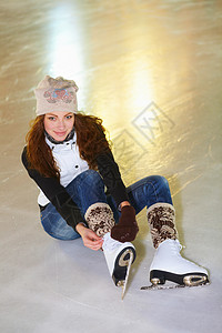 一位迷人的年轻女士坐在冰场上 绑着她冰鞋的丝带 她从雪橇上爬下来图片