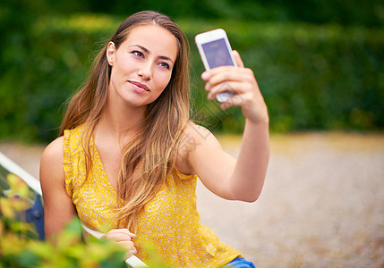 一个无忧无虑的年轻女子 在公园用手机拍自拍 玩个不停图片