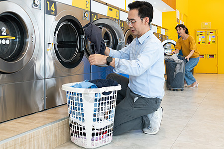 亚洲人使用合格的洗衣机 在公共房间里商业自助男人硬币女性男性篮子洗涤剂家务成人图片