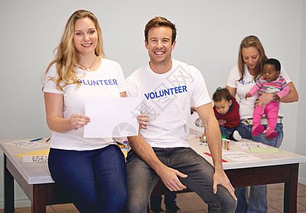 我们热爱向社区回馈 志愿者在与幼儿一起工作时拿着一个空白的牌子 (笑声)图片