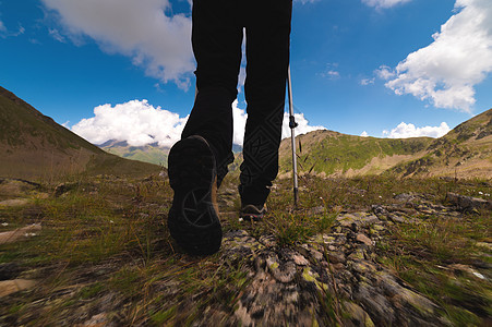 一位身穿黑色裤子和带登山杖的登山鞋的运动女性的腿在山上高高行走图片