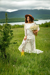 一位身穿白色连衣裙和棕色帽子的中年妇女手里拿着一个篮子 上面放着一大束雏菊 祝贺的野花花瓣洋甘菊天空生活荒野甘菊乡村园艺季节草地图片